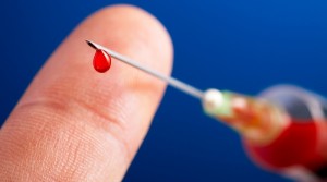 syringe needle with droplet of blood in front of a finger and on blue bacjground